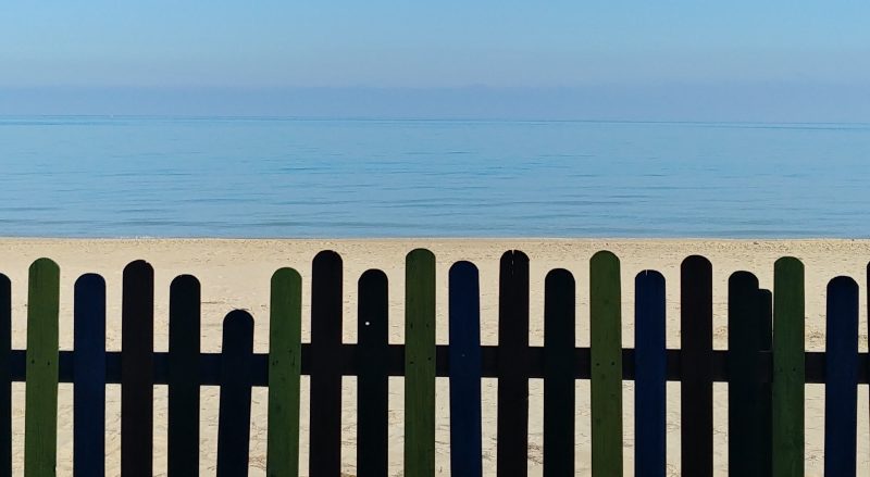 Uno steccato scuro, dietro al quale si vede la sabbia, e poi il mare azzurro. Per noi rappresenta il tono di voce, la personalità
